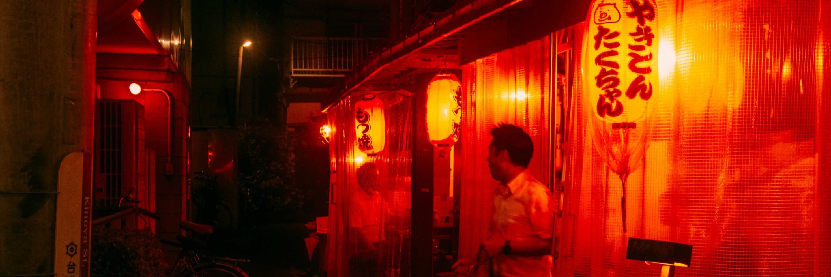 Night street scene with glowing red lanterns outside a Japanese eatery.